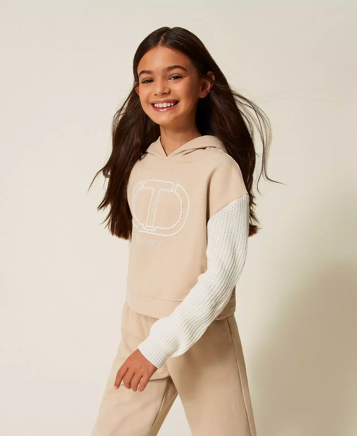 Pierrot Outlet TWINSET zandkleurige hoodie met witte gebreide mouwen en geborduurd logo gedragen door een meisje