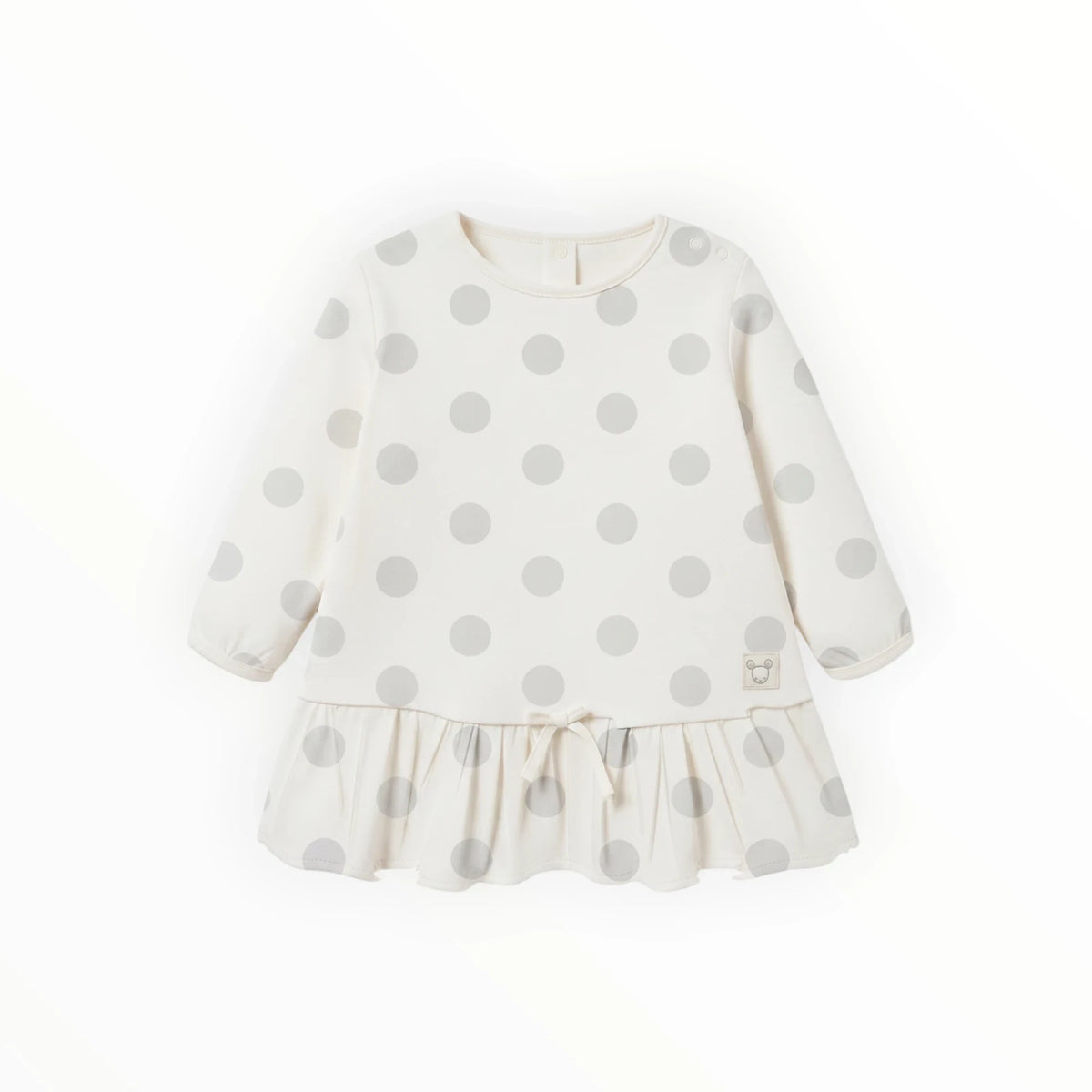 Pierrot Outlet babyjurk met lange mouwen, beige met grijze stippenprint, ruches aan de onderzijde en strikdetail.