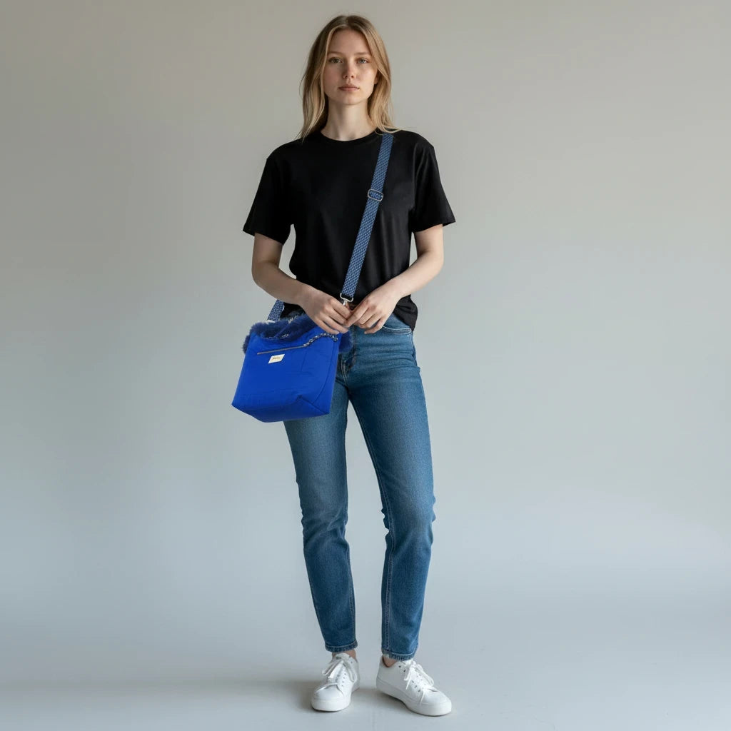 Model draagt een blauwe Bellerose gewatteerde schoudertas met imitatiebont en voorvak, gecombineerd met casual kleding.