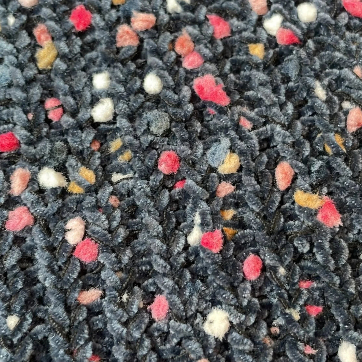 Close-up van de donkerblauwe gebreide stof van een Pierrot Outlet trui met kleurrijke roze, witte en okergele spikkels