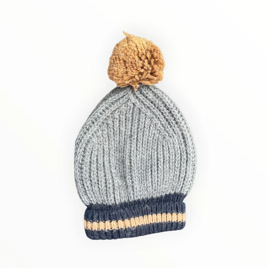 Pierrot Outlet grey ribbed knit winter beanie with a navy cuff, tan stripe, and a fluffy tan pom-pom on top.