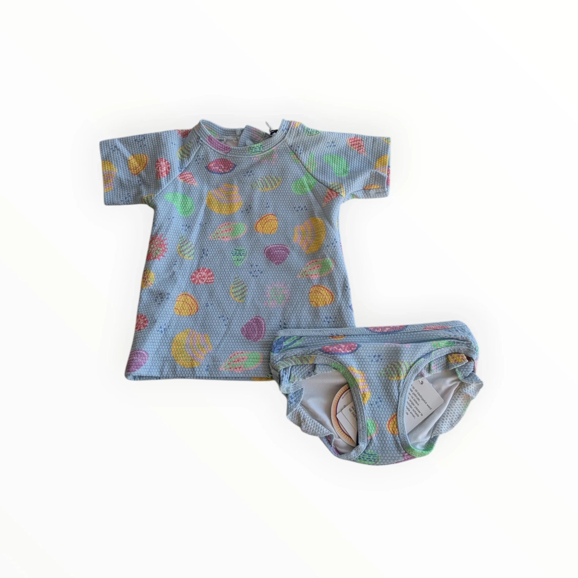Pierrot Outlet zwemset met schelpenprint voor kinderen, bestaande uit een UV-shirt en broekje in lichtblauw met veelkleurige schelpen.