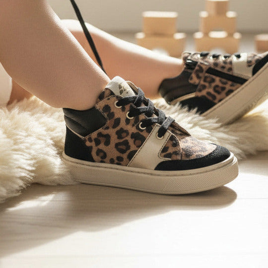 Pierrot Outlet kindersneakers met luipaardprint, zwarte details en goudkleurige accenten op een zacht schapenvachtkleed.