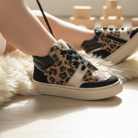Pierrot Outlet kindersneakers met luipaardprint, zwarte details en goudkleurige accenten op een zacht schapenvachtkleed.