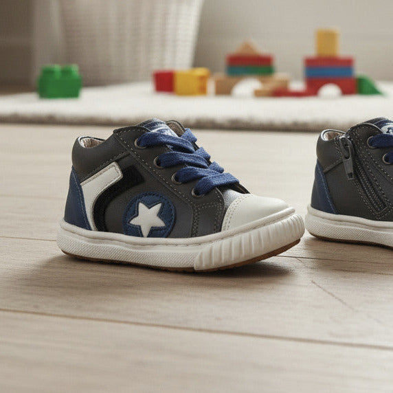 Pierrot Outlet leren babysneakers in grijs en blauw met ster-detail, veters en ritssluiting op een houten vloer.