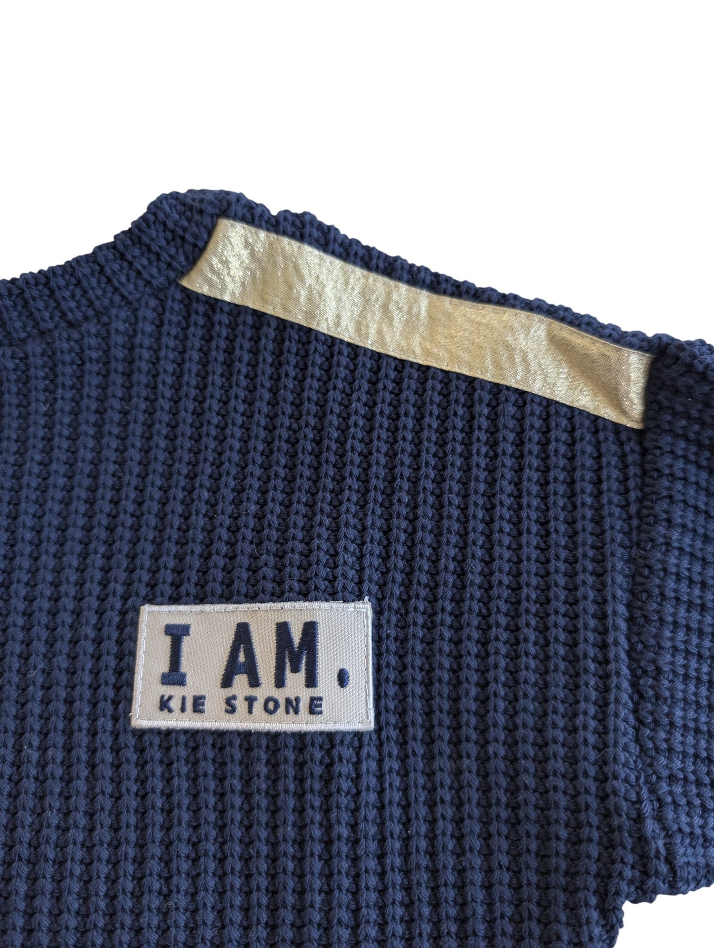 Pierrot Outlet navyblauwe gebreide trui met lange mouwen, gouden schouderband en patch met tekst 'I. AM. KIE STONE'.