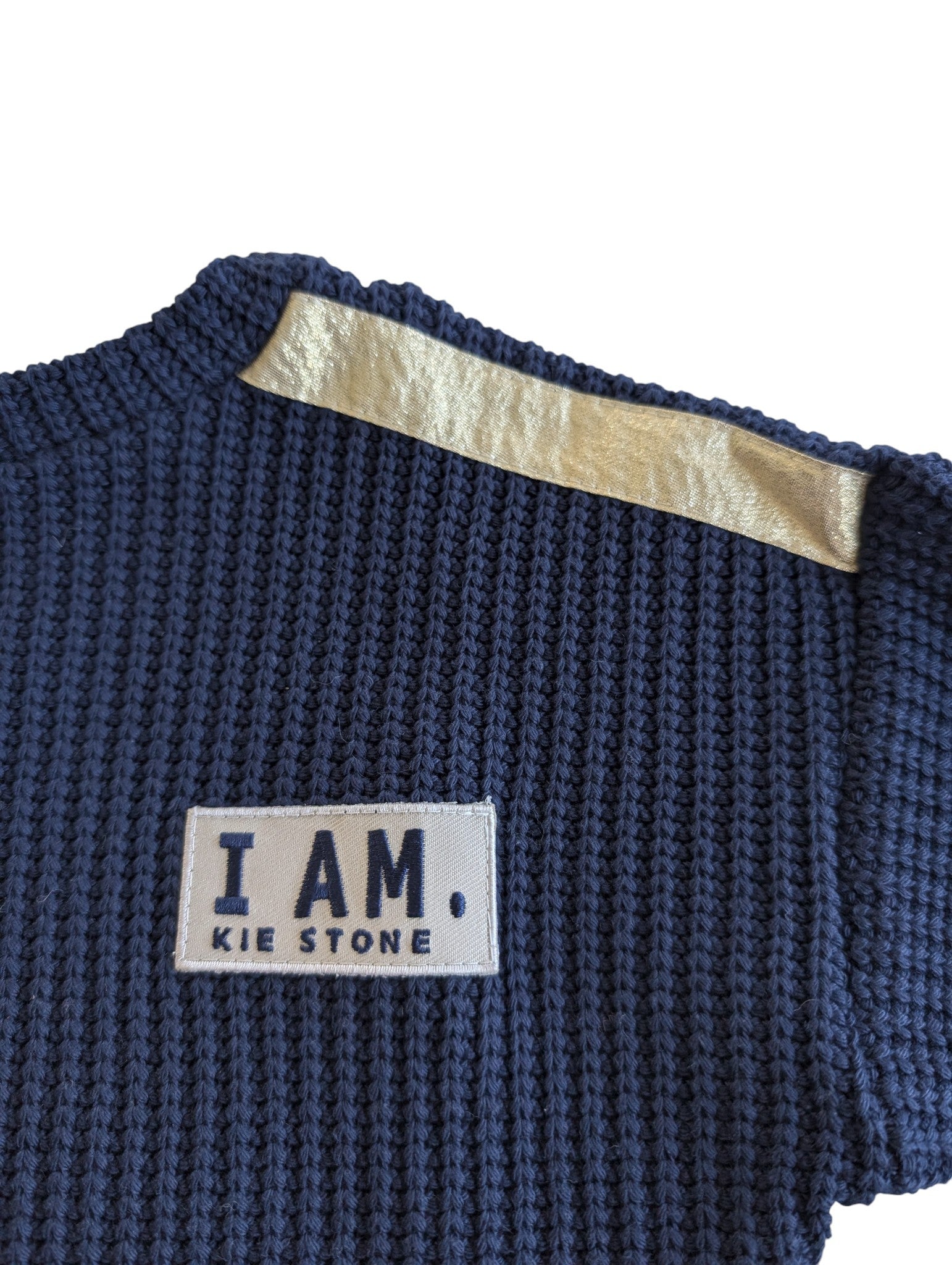 Pierrot Outlet navyblauwe gebreide trui met lange mouwen, gouden schouderband en patch met tekst 'I. AM. KIE STONE'.