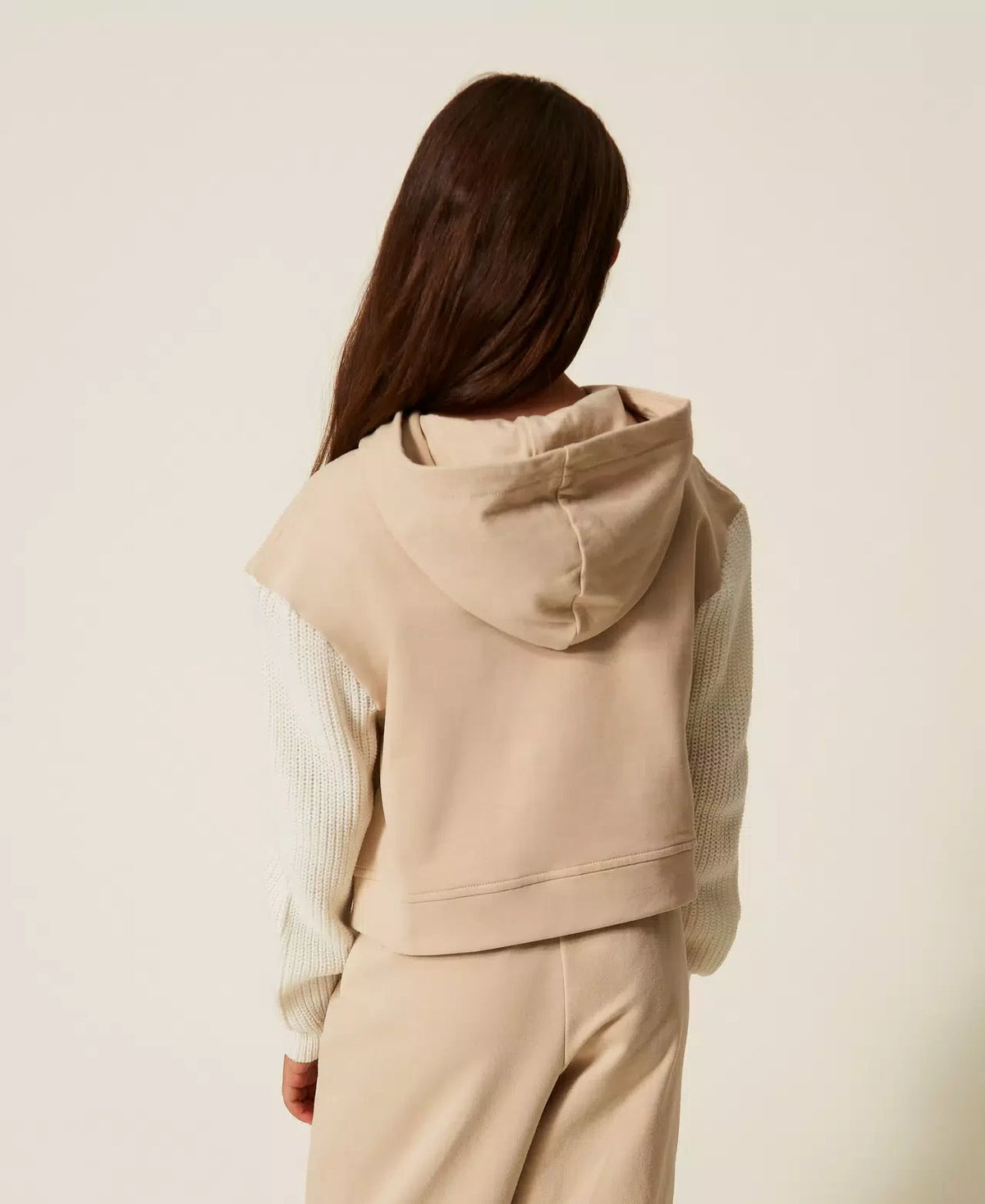 Achterkant van een zandkleurige TWINSET hoodie met witte gebreide mouwen en capuchon, gedragen door een meisje.