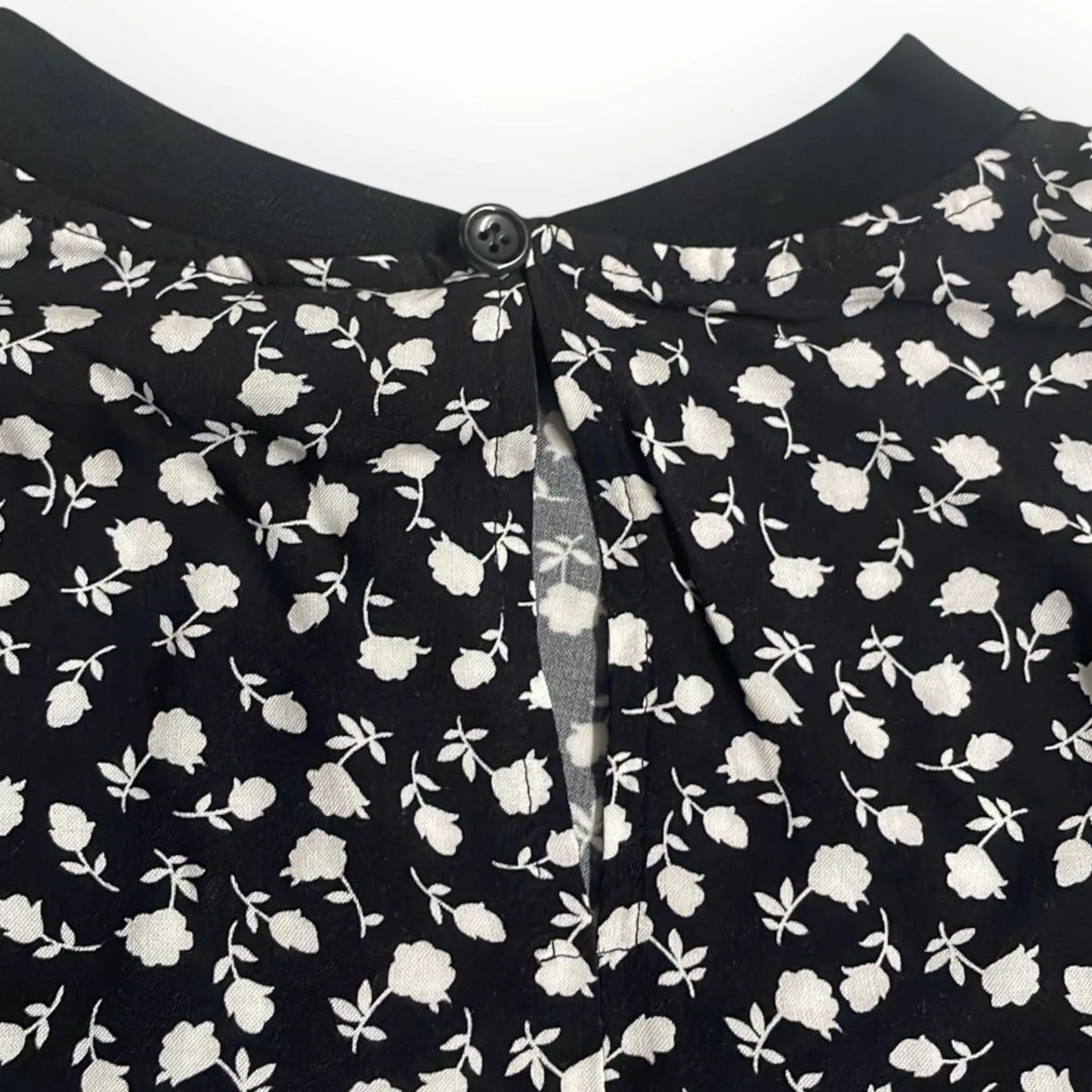 Pierrot Outlet damesblouse met zwarte basis en wit bloemenmotief, voorzien van een subtiele knoopsluiting in de nek.