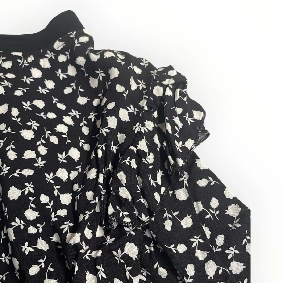Pierrot Outlet damesblouse in zwart met wit bloemmotief, voorzien van elegante ruches op de schouders.